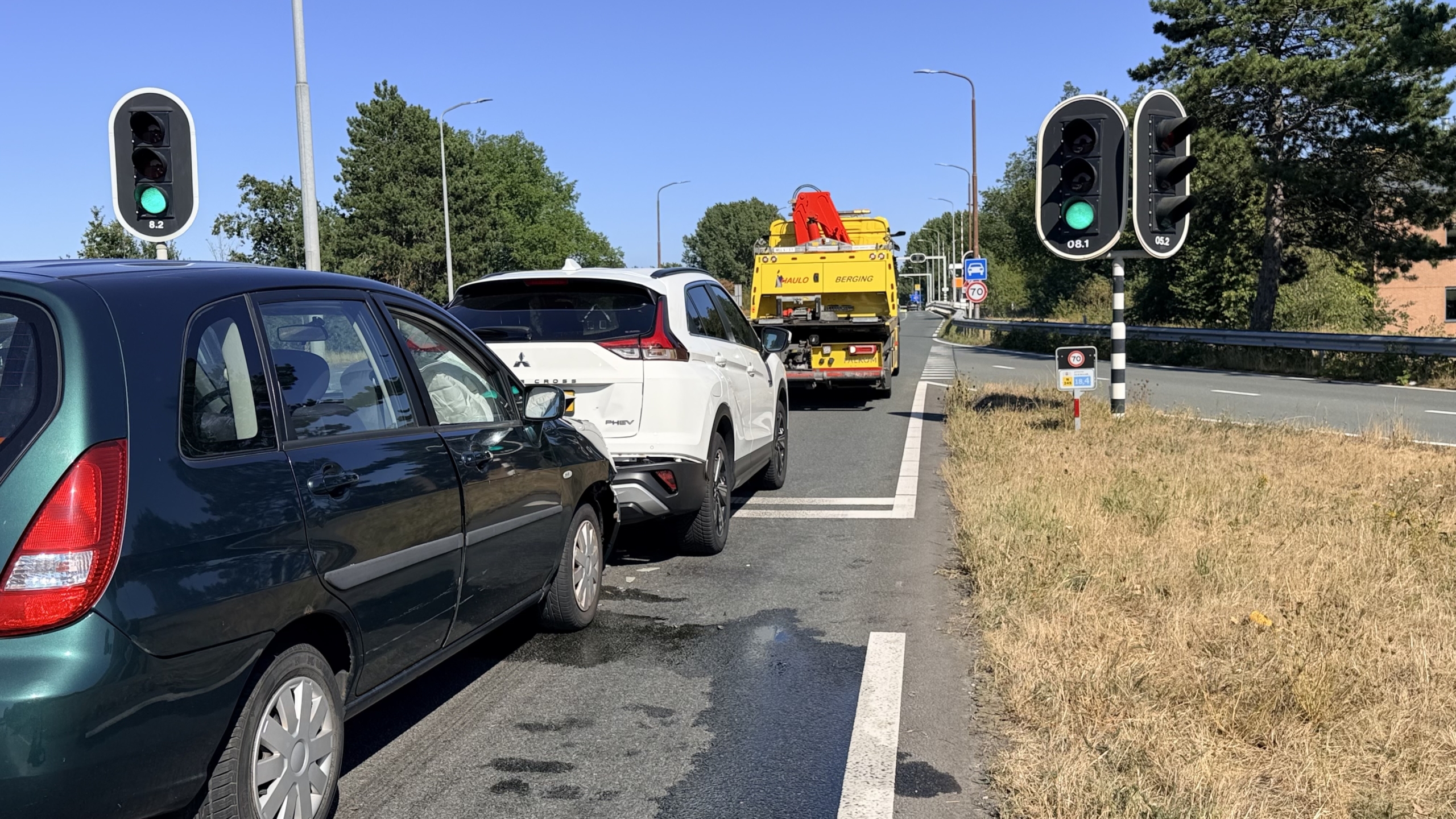 Ambulance naast botsing waarbij een groene auto achterop een witte SUV is gereden op een kruising