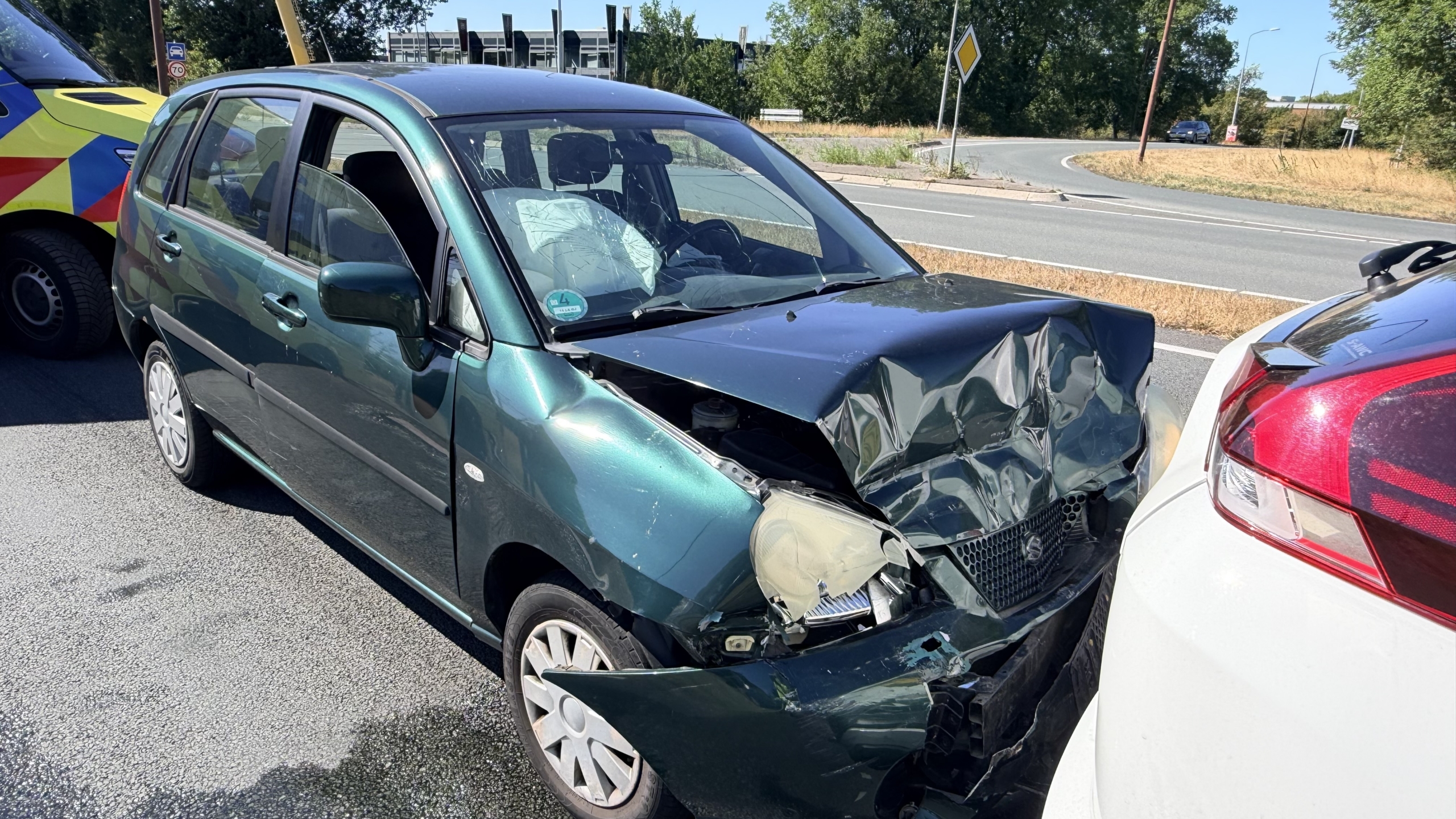Ambulance naast botsing waarbij een groene auto achterop een witte SUV is gereden op een kruising