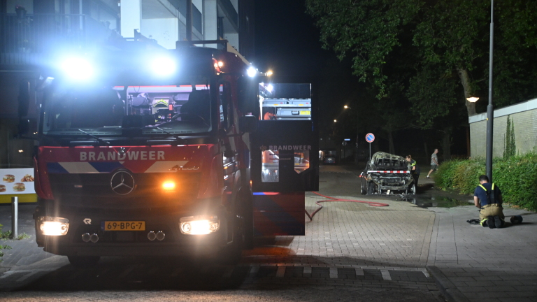 Brandweerman blust brandende auto met zwaar beschadigde voorkant, met open motorkap en rook in het donker
