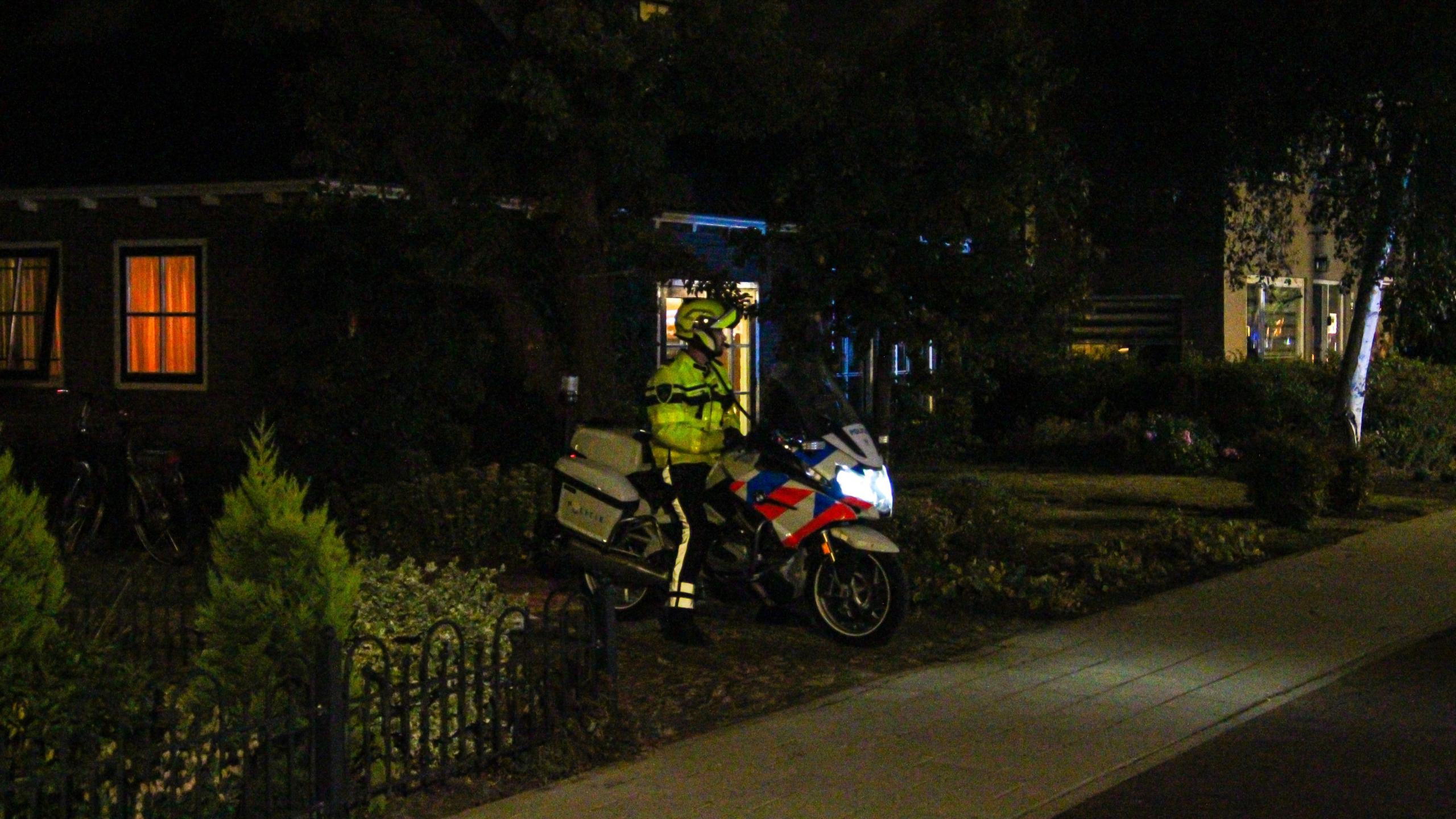Politieauto met felle koplampen op een donkere straat, met een persoon lopend en een rood-wit gestreepte wagen op de voorgrond