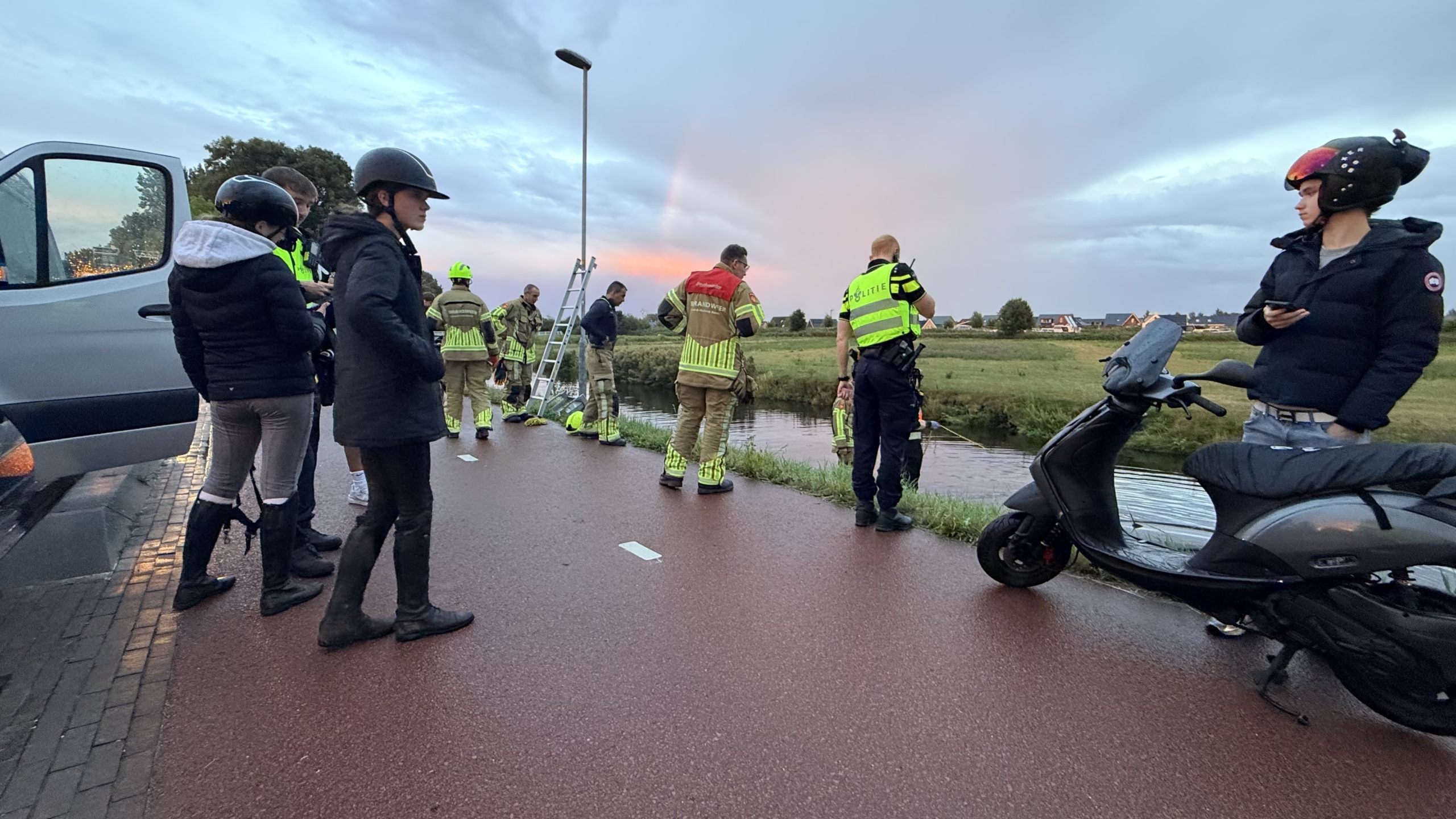 Hulpdiensten in fluorescerende jassen bergen een half ondergelopen auto uit een sloot langs een grasdijk