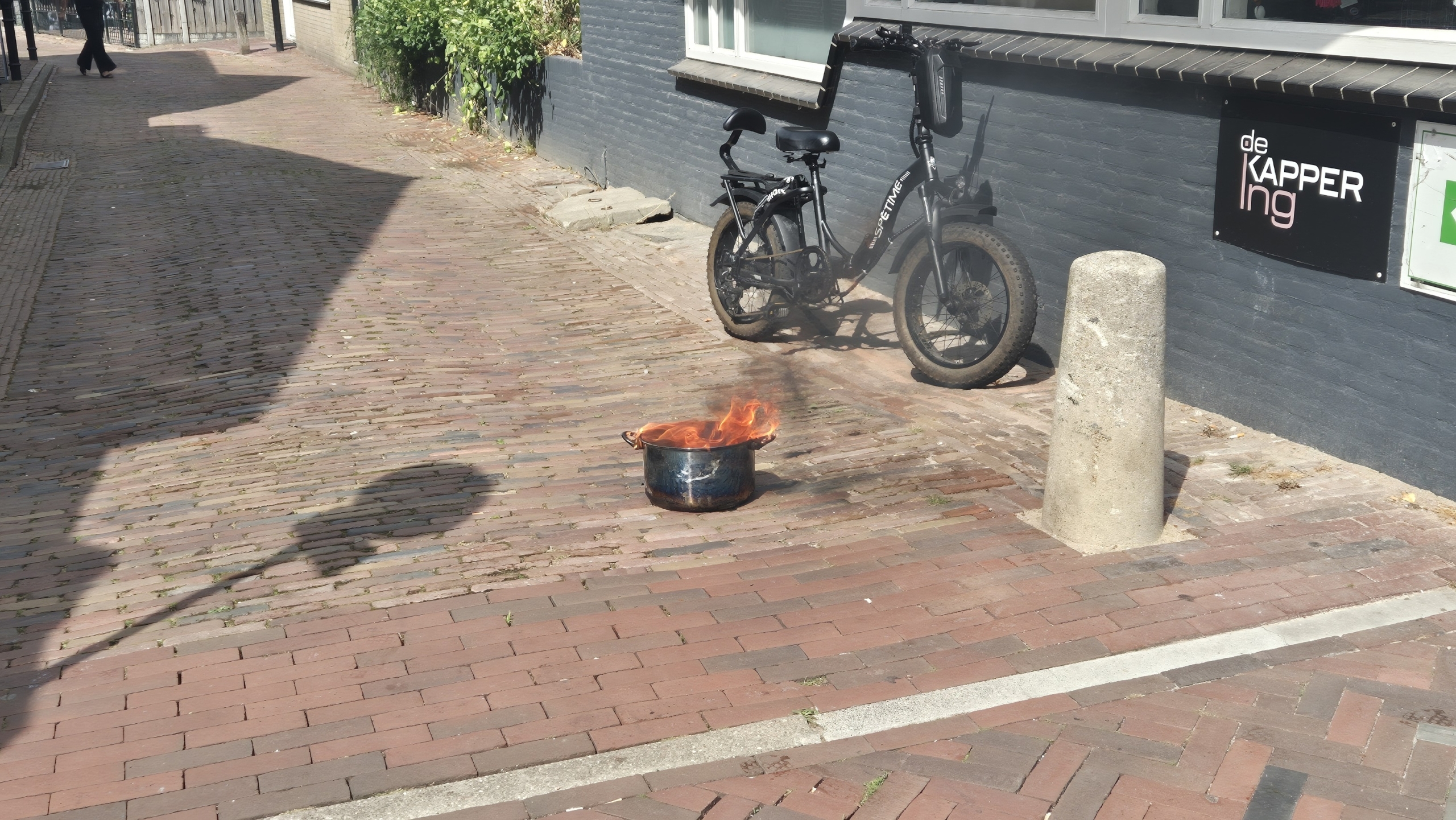 Brandweerwagen geparkeerd voor Huna AL-Yemen Restaurant naast een kapperszaak, met enkele mensen bij de ingang