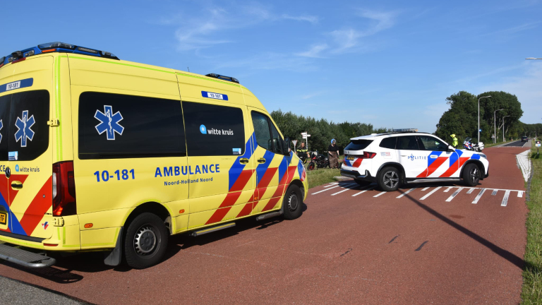 Ambulance en politieauto blokkeren een fietspad langs de weg bij een ongeval, met hulpverleners op de achtergrond