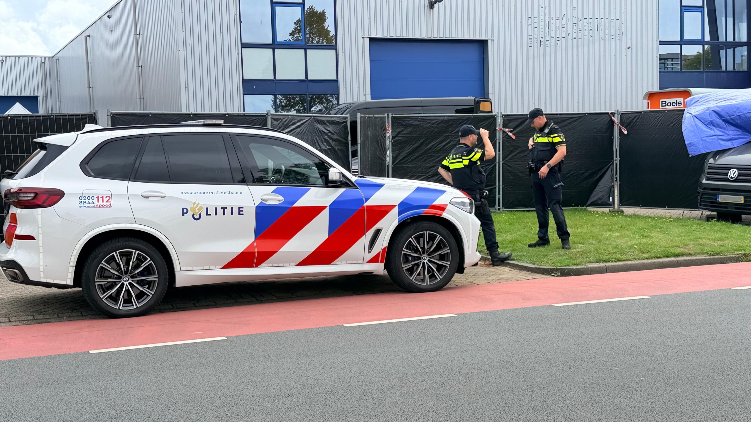 Politieagenten bij een grijze bestelbus met blauw zeil op een bedrijventerrein, met politieauto op de voorgrond