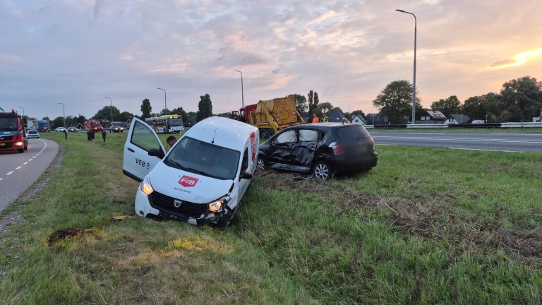 Twee beschadigde auto’s in de berm na aanrijding langs de snelweg, met hulpdiensten en verkeer op de achtergrond