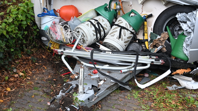 Zwaar beschadigde caravan met ingedeukte voorkant na aanrijding, met een auto op de voorgrond in een woonstraat
