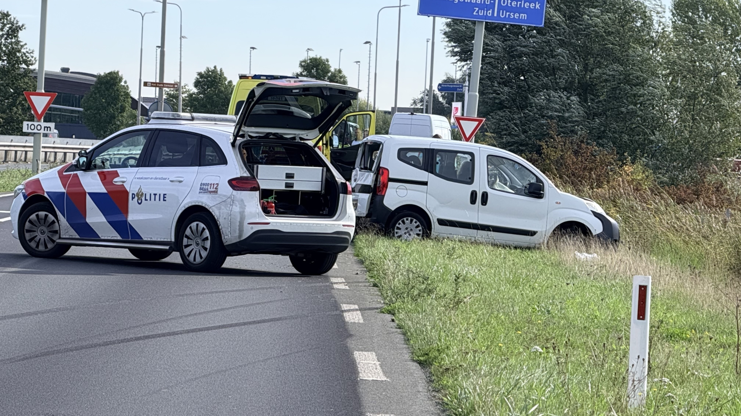 Beschadigde witte bestelwagen in de berm, met verspreide spullen in het gras en een politieauto op de achtergrond