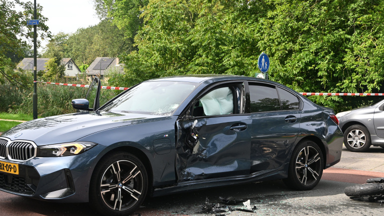 Hulpverleners en politie verlenen eerste hulp bij een verkeersongeluk naast een auto, met brancard en ambulance op de weg