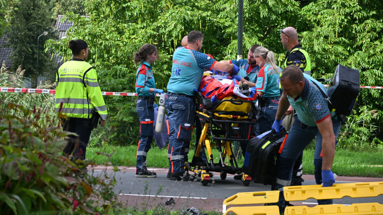 Hulpverleners en politie verlenen eerste hulp bij een verkeersongeluk naast een auto, met brancard en ambulance op de weg