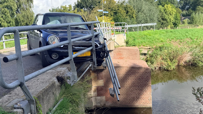 Zwarte auto tegen de leuning van een brug gereden, met verbogen metalen hekwerk boven het water