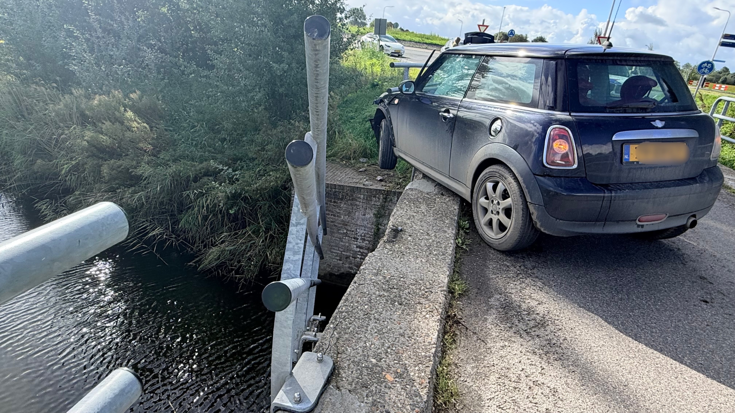 Zwarte auto tegen de leuning van een brug gereden, met verbogen metalen hekwerk boven het water