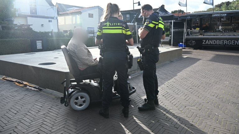 Twee politieagenten bij een wit busje, met op de achtergrond een ambulance in een woonstraat met afzetborden
