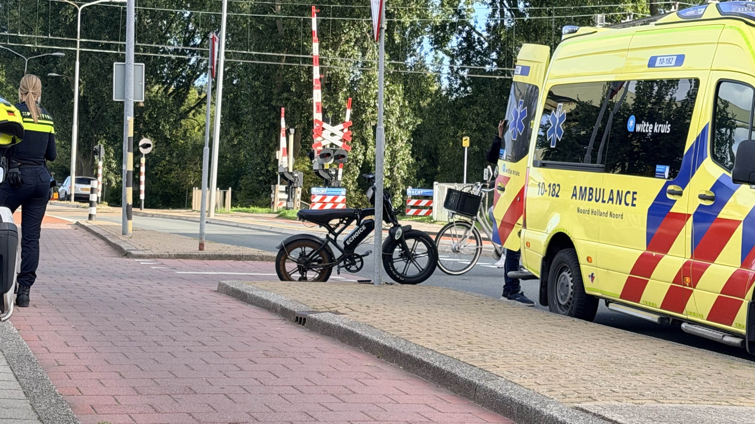 Politie en hulpverleners helpen een persoon bij een e-bike naast een ambulance op straat