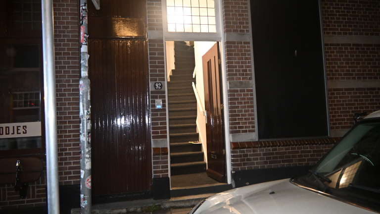 Brandweerlieden en politie op straat bij een hoekpand in de nacht, met brandweerwagen, slangen en fietsen op de voorgrond