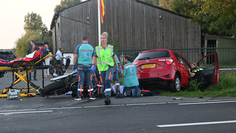 Hulpdiensten bij verkeersongeval: ambulancepersoneel bij omgevallen motor en rode auto langs de weg