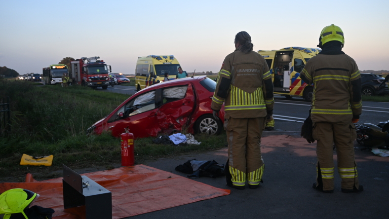 Hulpdiensten bij verkeersongeval: ambulancepersoneel bij omgevallen motor en rode auto langs de weg