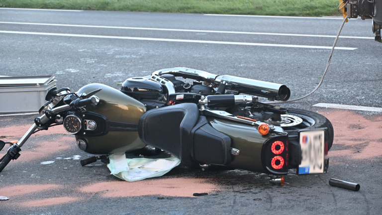 Hulpdiensten bij verkeersongeval: ambulancepersoneel bij omgevallen motor en rode auto langs de weg