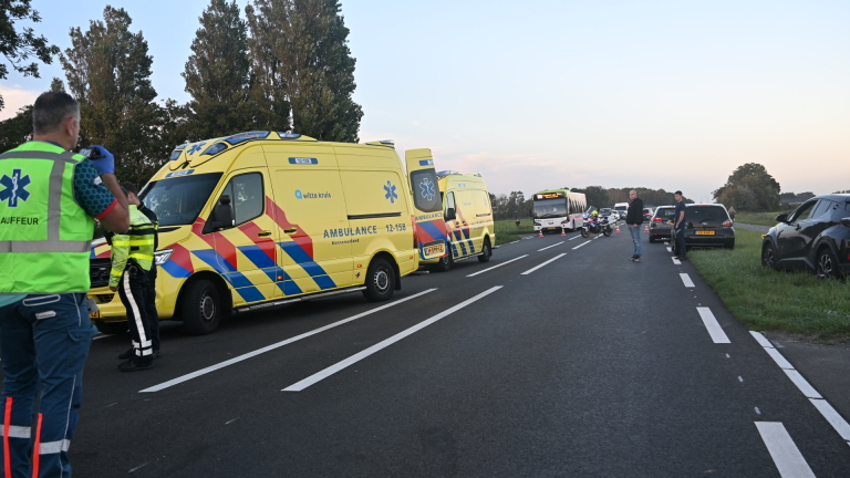 Hulpdiensten bij verkeersongeval: ambulancepersoneel bij omgevallen motor en rode auto langs de weg
