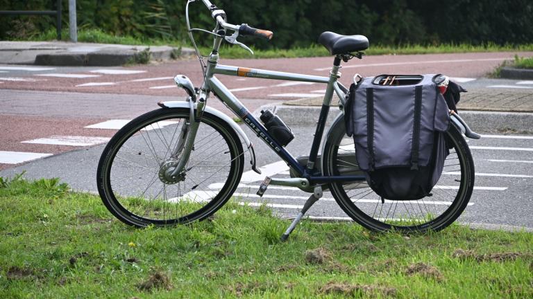 Gele ambulance met open zijdeur; politieagent staat ernaast langs een weg met groen en bordje Dijkweg