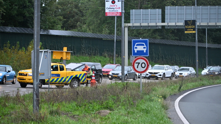 Beschadigde lichtblauwe auto wordt weggesleept na ongeval, met Nederlandse politieauto’s en agenten op kruispunt