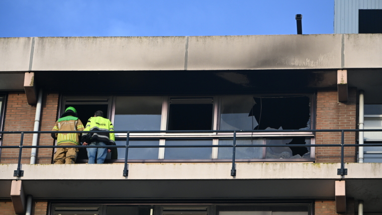 Brandweerman en medewerker inspecteren een door brand beschadigd balkon met roetsporen en kapotte ramen