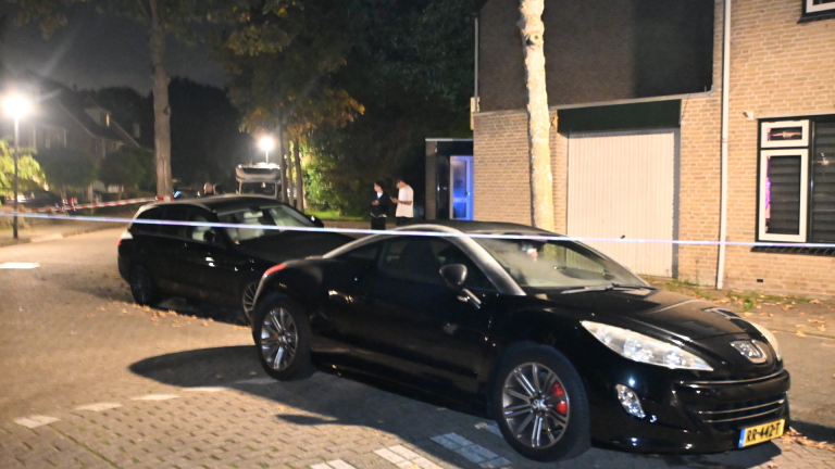 Ruit van woning met jaloezieën en twee kogelgaten in het glas, naast bakstenen muur en raamkozijnen