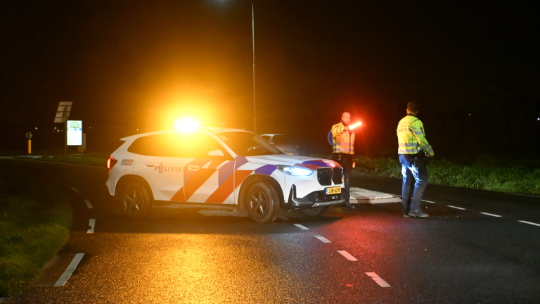 Auto in de berm langs een sloot, met een hulpverlener in oranje reflectiekleding bij het voertuig in de nacht