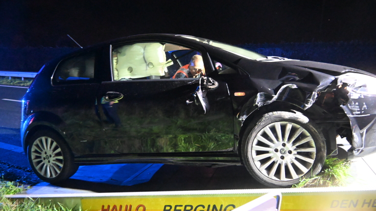 Zwarte auto na aanrijding langs de weg, met uitgeklapte airbag en schade aan de linker voorkant, in blauw zwaailicht