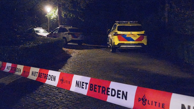 Politieauto en agenten op een donker bospad achter rood-wit lint met tekst ‘NIET BETREDEN’