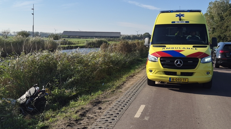 Motorfiets ligt omgevallen tussen hoog riet en gras langs de waterkant, met zichtbaar achterwiel en kenteken