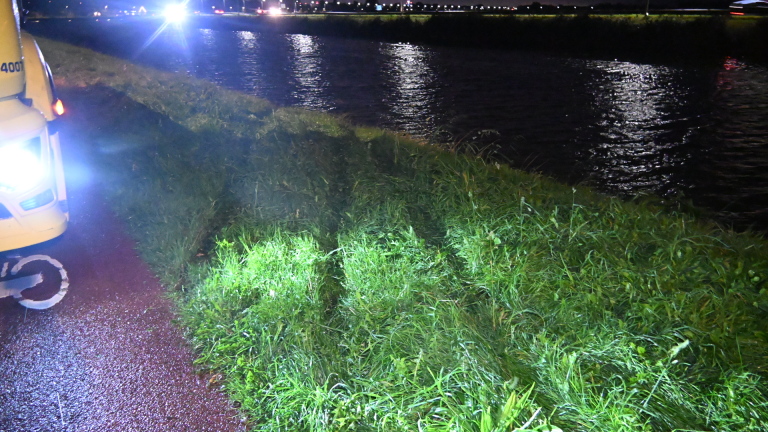 Bergingswagen en politieauto met zwaailichten op natte weg in de nacht, met hulpverleners ernaast