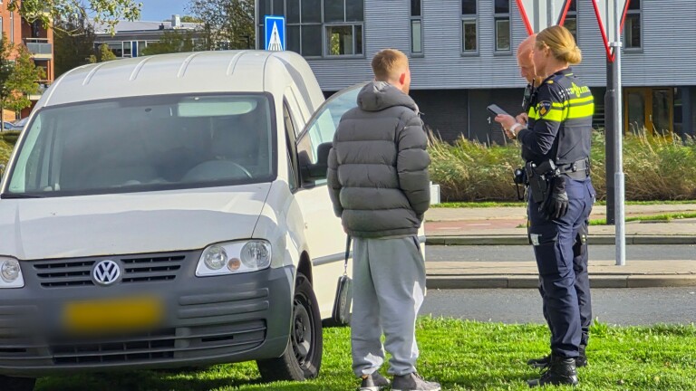 Gele ambulance van Witte Kruis geparkeerd bij een zebrapad langs een weg met bomen en auto’s